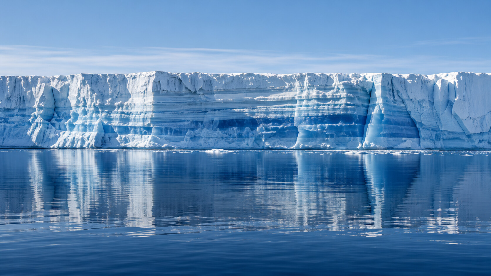 The layered face of an ice shelf, built up over many years, above still water.